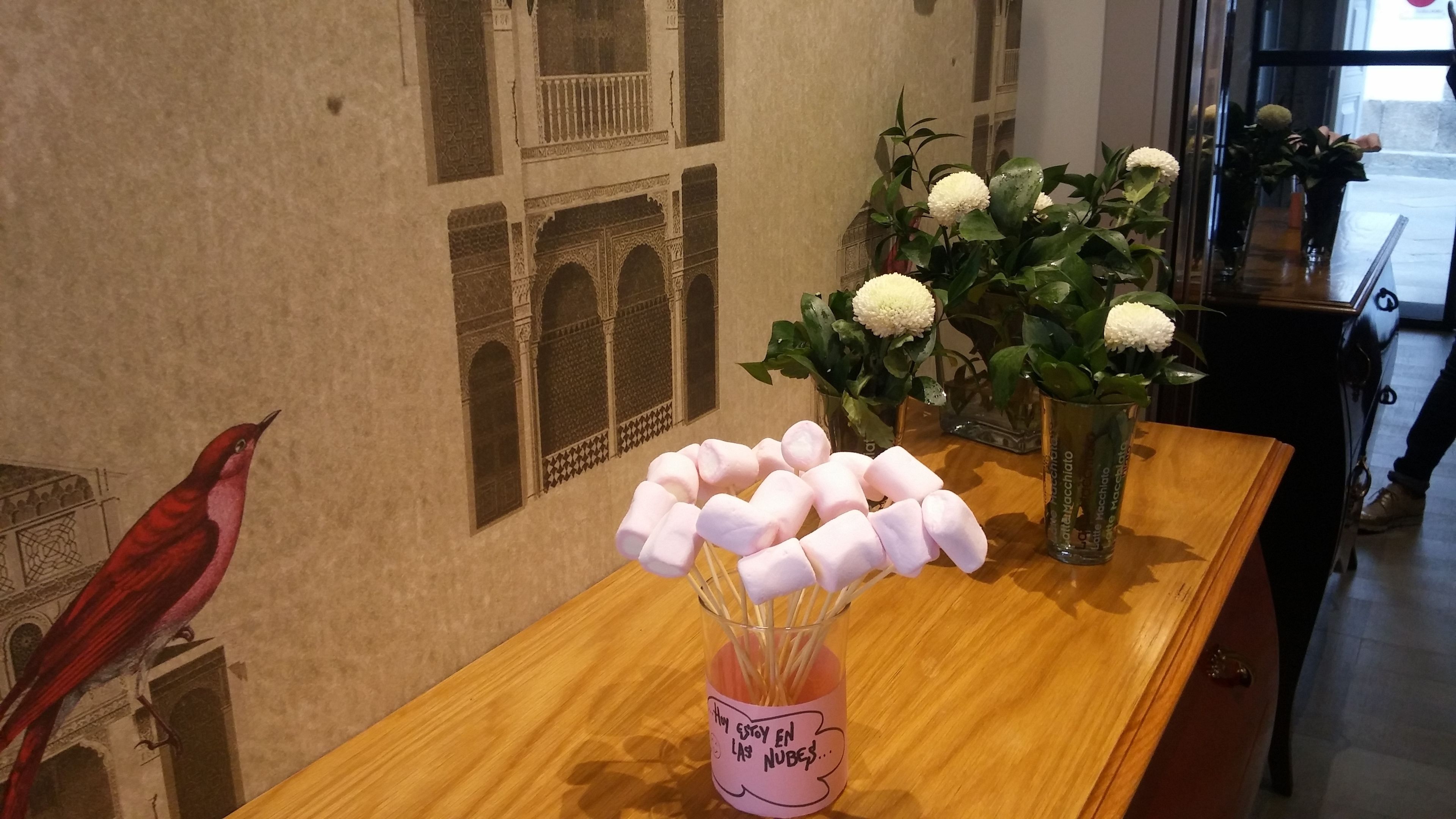 Een houten tafel met een glazen vaas met witte bloemen en een roze bakje met marshmallows.