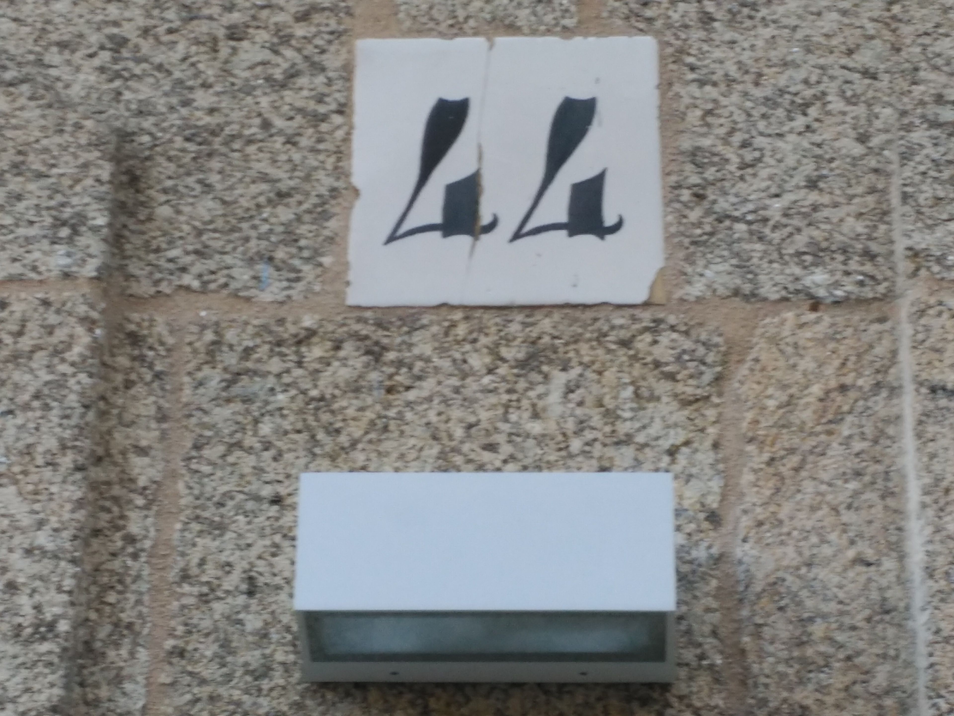 A wall with two signs: one with a black symbol and another with a white rectangular shape.
