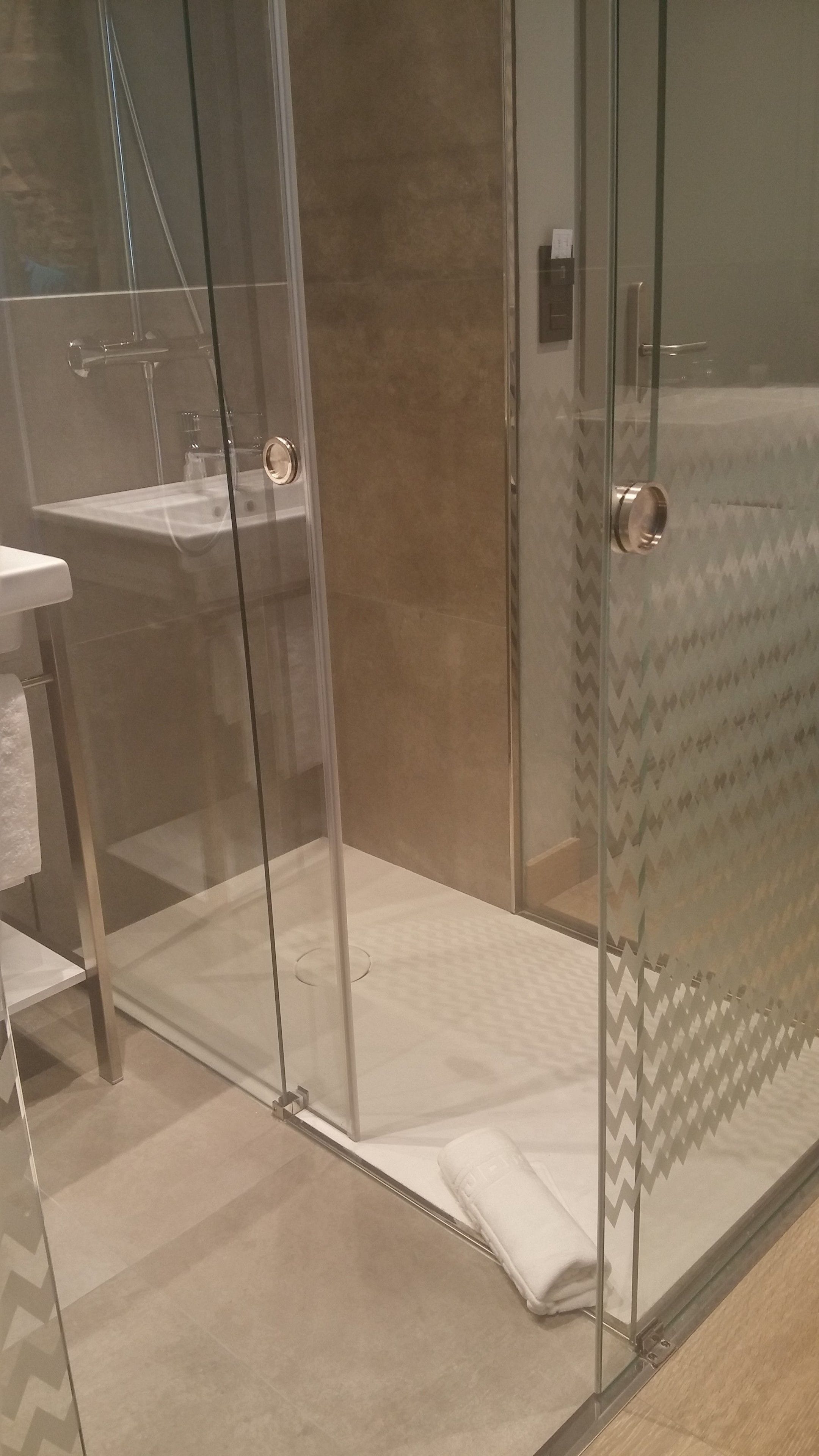 A glass-enclosed shower area with a white towel on the floor, a glass door, and a showerhead visible through the glass.