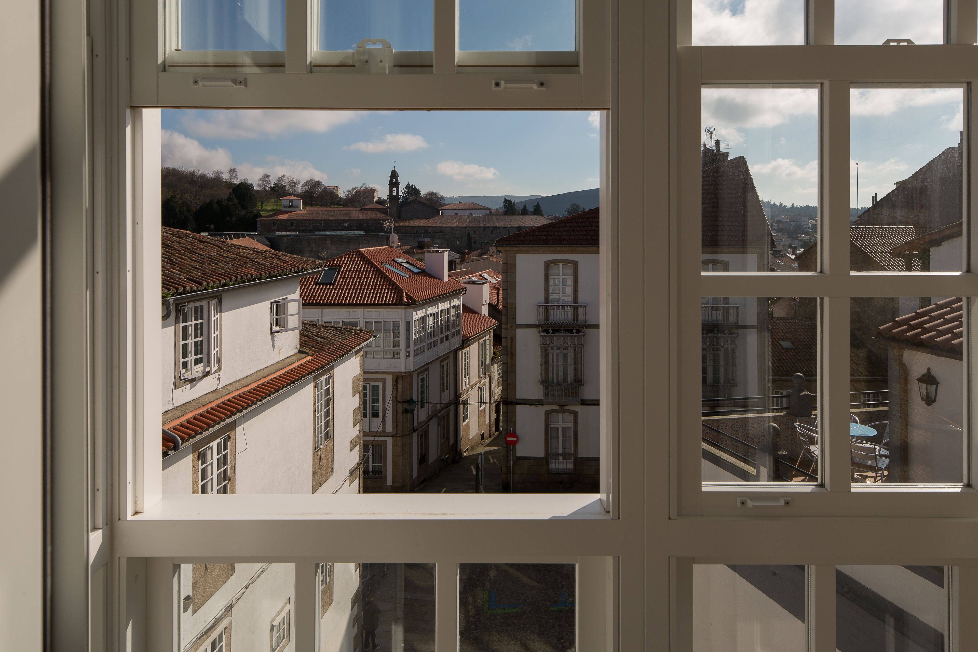 Une vue à travers la fenêtre d’un immeuble à plusieurs étages, présentant une architecture traditionnelle avec des toits en tuiles et un mélange de balcons et de fenêtres.