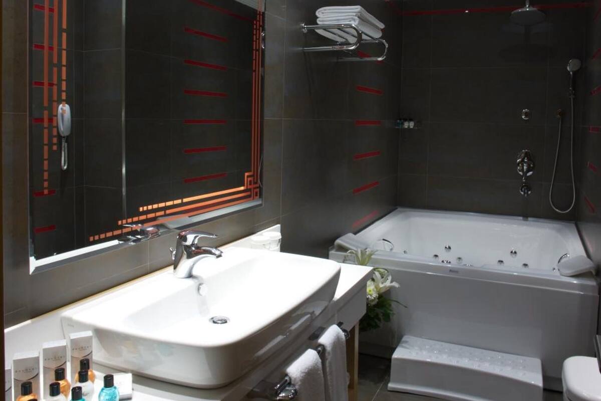 A modern bathroom with a large mirror, a bathtub, and a vanity with a sink and toiletries.