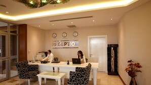 A reception area with a reception desk, two chairs, a coffee machine, and a clock on the wall. - dovsOtel (Manisa)