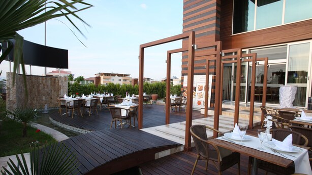 An outdoor dining area with wooden tables and chairs, a small water feature, and a view of the surrounding buildings. - dovsOtel (Manisa)