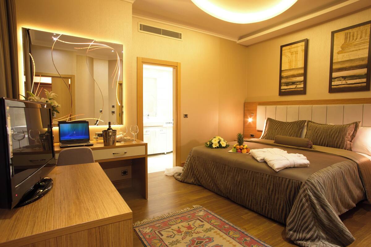 A hotel room with a bed, desk, computer, and a mirror.