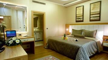A hotel room with a bed, bedside tables, a desk with a computer, a mirror, and artwork on the walls.