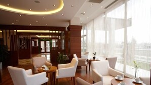 A modern hotel lobby with a wooden floor, white leather sofas, and round tables. - dovsOtel (Manisa)