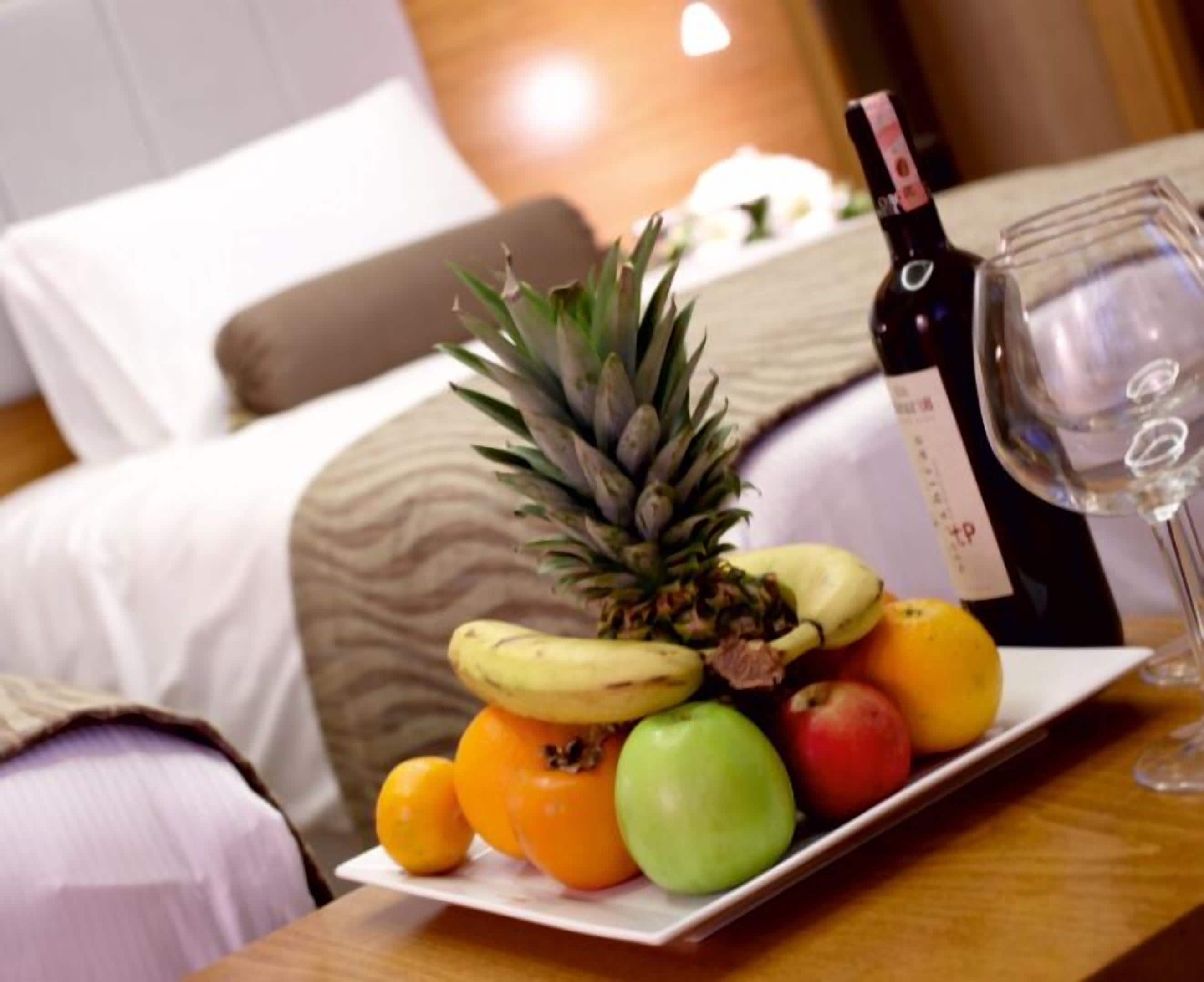 Uma tábua de frutas bem organizada, uma garrafa de vinho e um copo sobre a mesa de um quarto de hotel.
