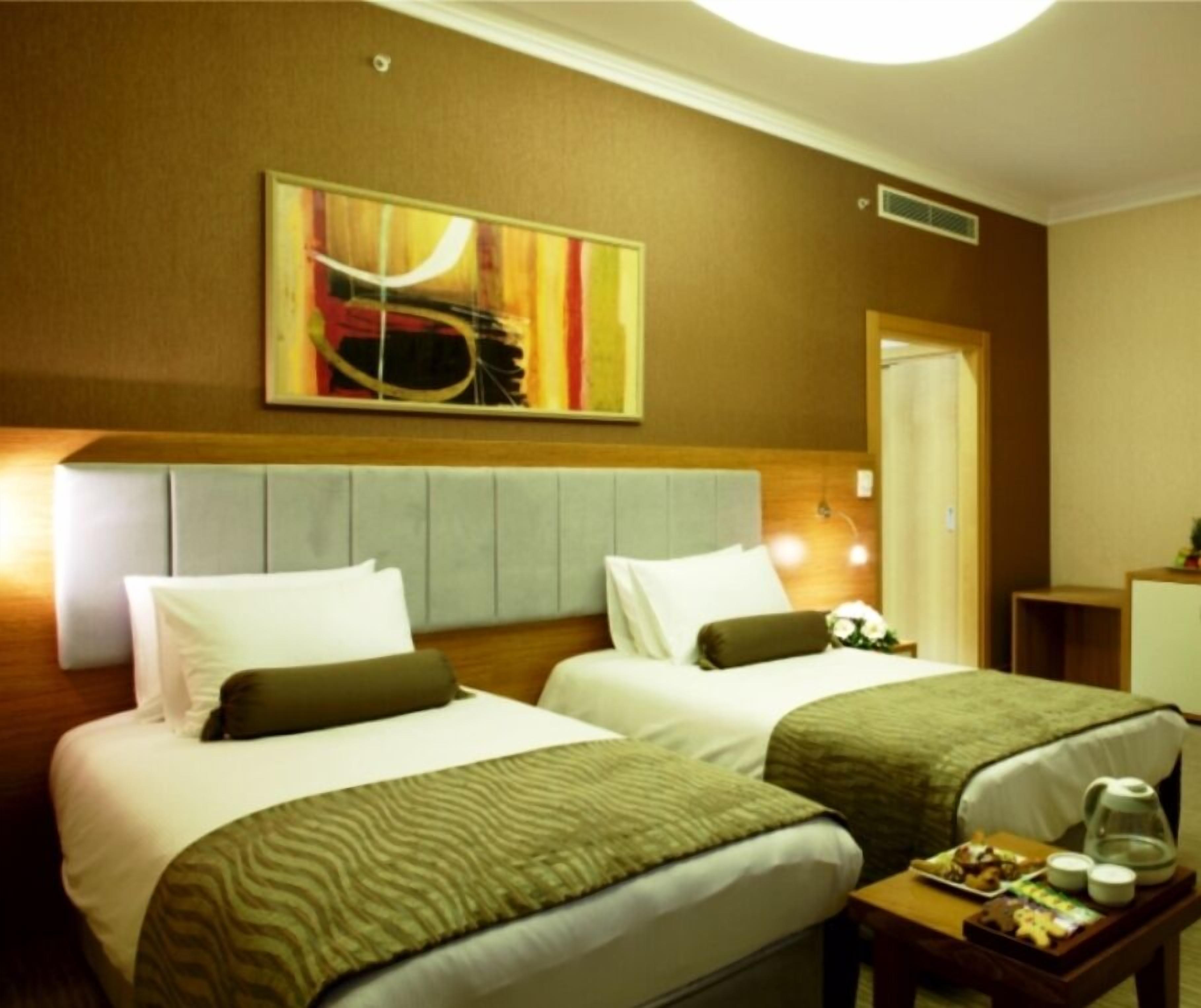 Une chambre d’hôtel avec deux lits, une tête de lit, un tableau, une table de chevet avec un plateau de nourriture et une petite table de nuit.