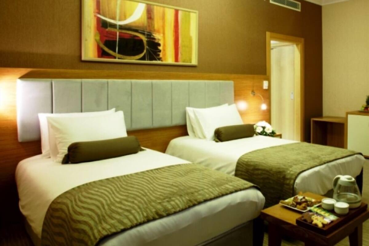 A hotel room with two beds, a headboard, a painting, a bedside table with a tray of food, and a nightstand.
