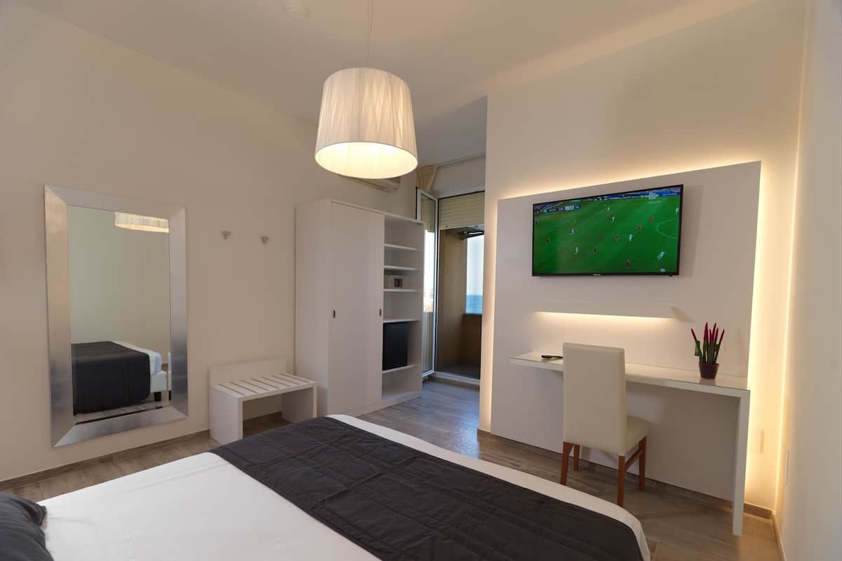 Una habitación de hotel moderna con una cama grande, un escritorio con una silla, un televisor montado en la pared y un armario.