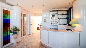 Una zona de recepción con piso de mármol, un mostrador curvo y un estante de pared con adornos.