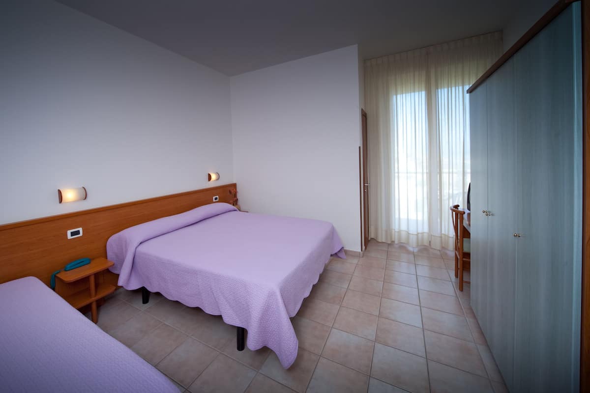 Una habitación de hotel con dos camas individuales, un cabecero de madera, una mesita de noche con lámpara y un armario.