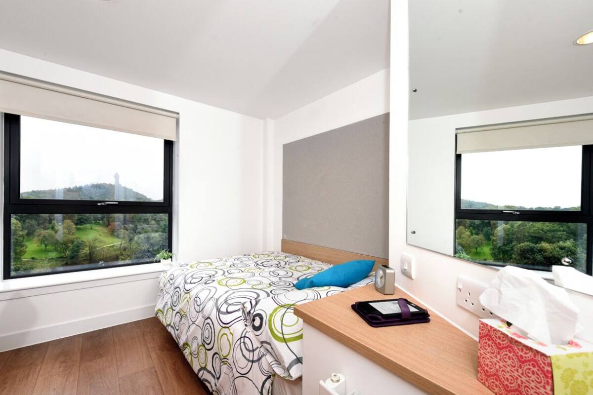 Habitación de hotel moderna con una cama grande, un escritorio de madera y una ventana con vistas a la ciudad.
