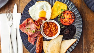 Un plato de comida para el desayuno que incluye huevos, tocino, salchichas, frijoles, tostadas y un tomate a la plancha.