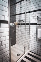 A modern bathroom with a glass-enclosed shower, white tiled walls, and a black and white striped floor.