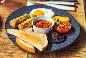 Ein Teller Frühstück mit Toast, Spiegeleiern, Bohnen, einer gegrillten Tomate und einem Pilz.