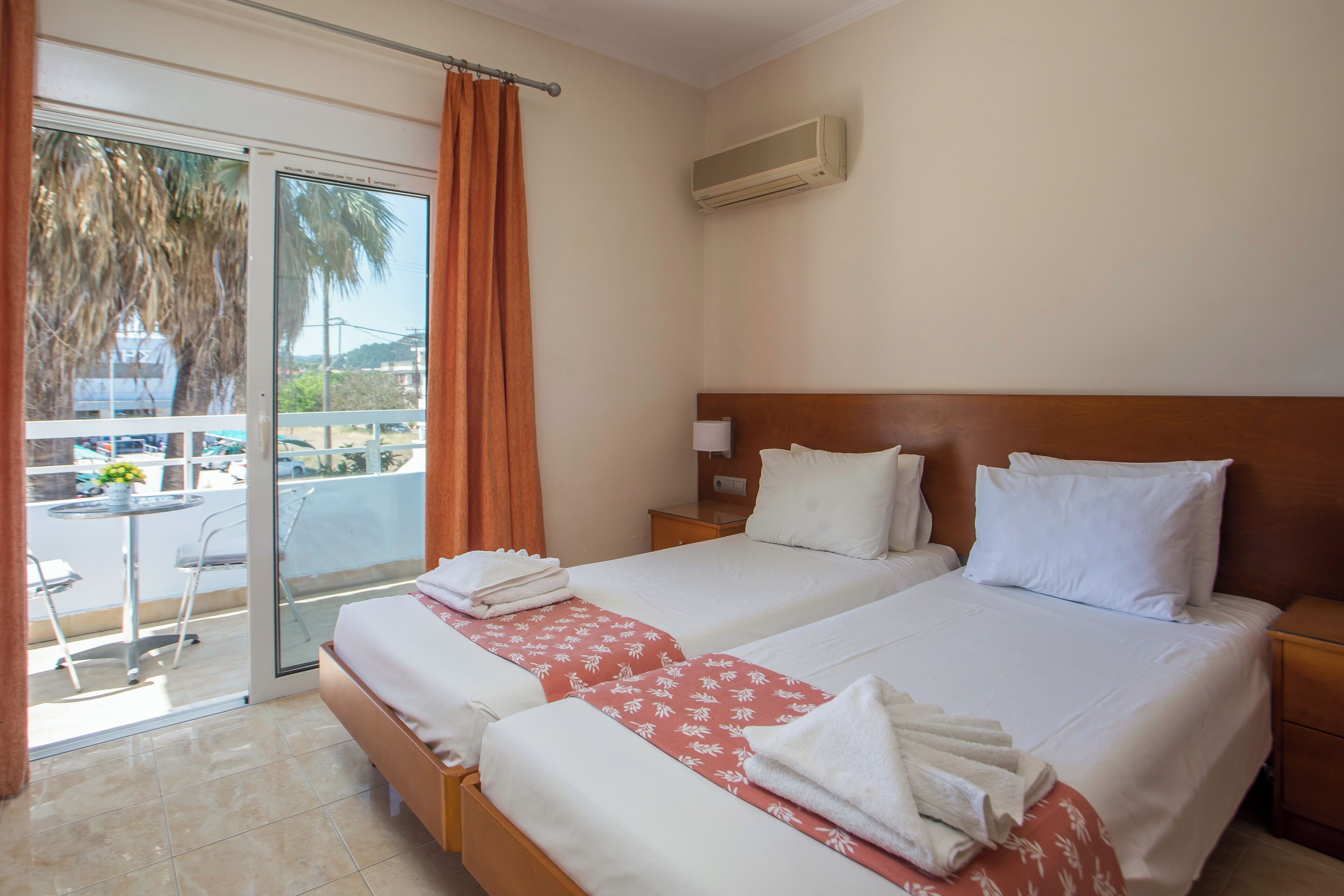 A hotel room with two beds, a balcony with a view, and an air conditioning unit.