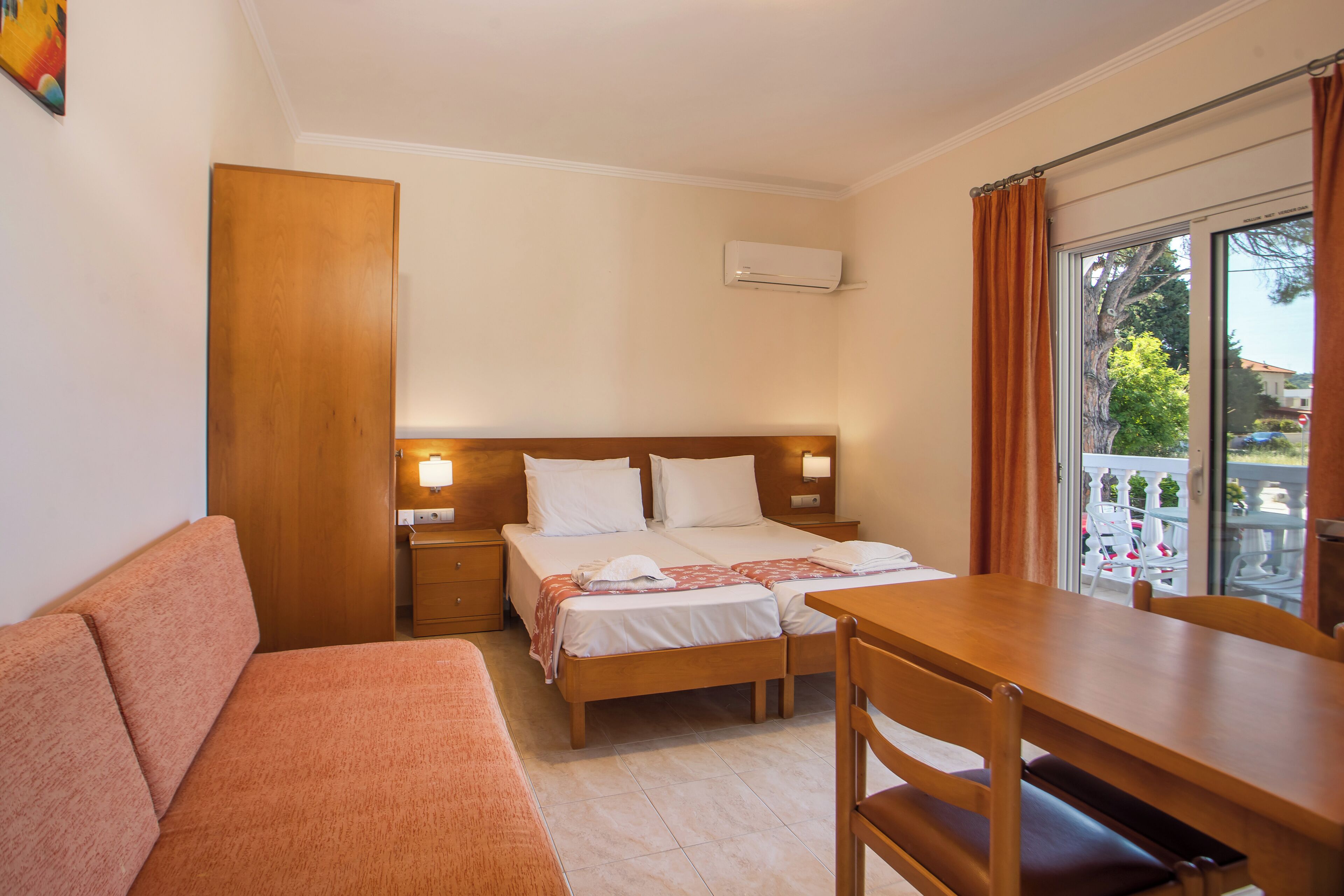 A hotel room with a bed, a sofa, a dining table, and a balcony with a view.