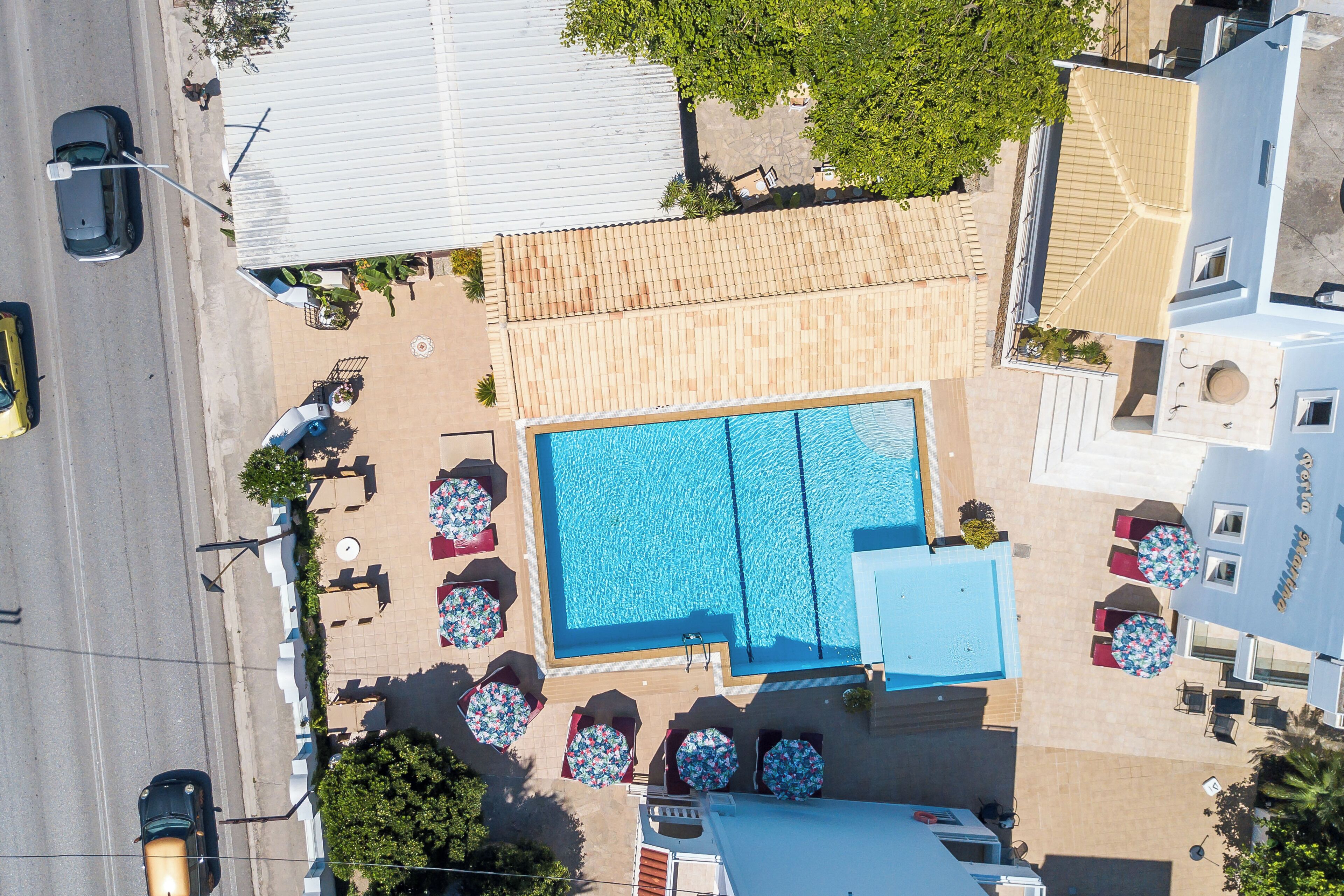 Vista aérea de un hotel con una piscina grande, mobiliario exterior y vista a la calle.