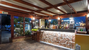 A bar area with a stone counter, wooden beams, and a view of the night outside. - Perla Marina (Rhodes)