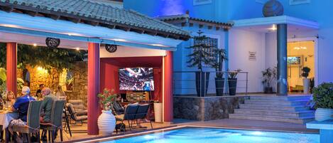 Zona de piscina con comedor y pantalla de televisión.