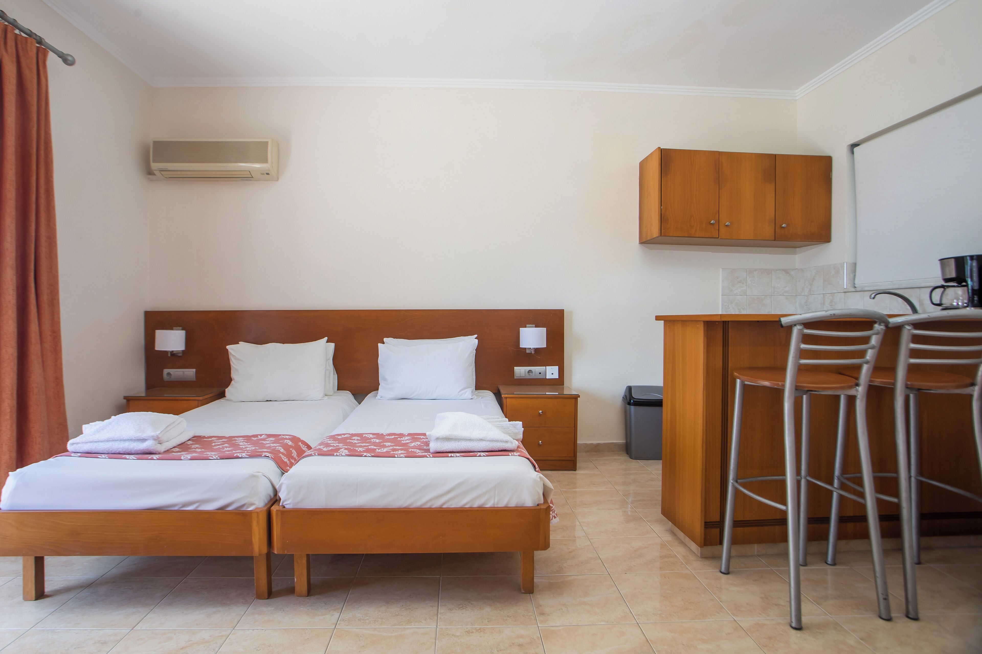Habitación de hotel con cama doble, un escritorio pequeño con silla, un armario de madera y un cubo de basura.