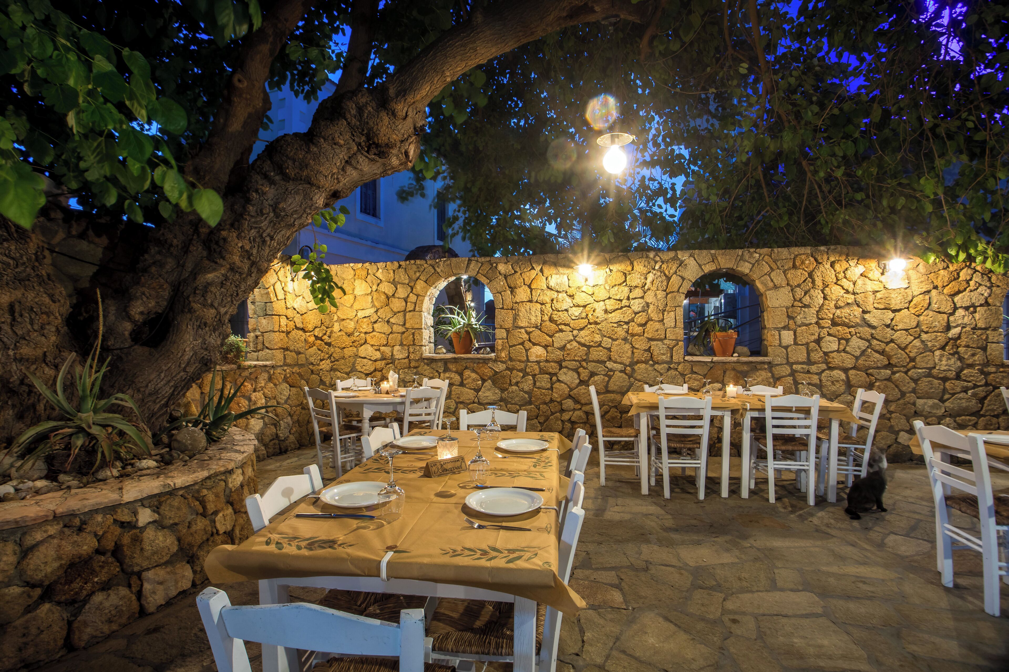 An outdoor dining area with stone walls, white chairs, and tables set for a meal.