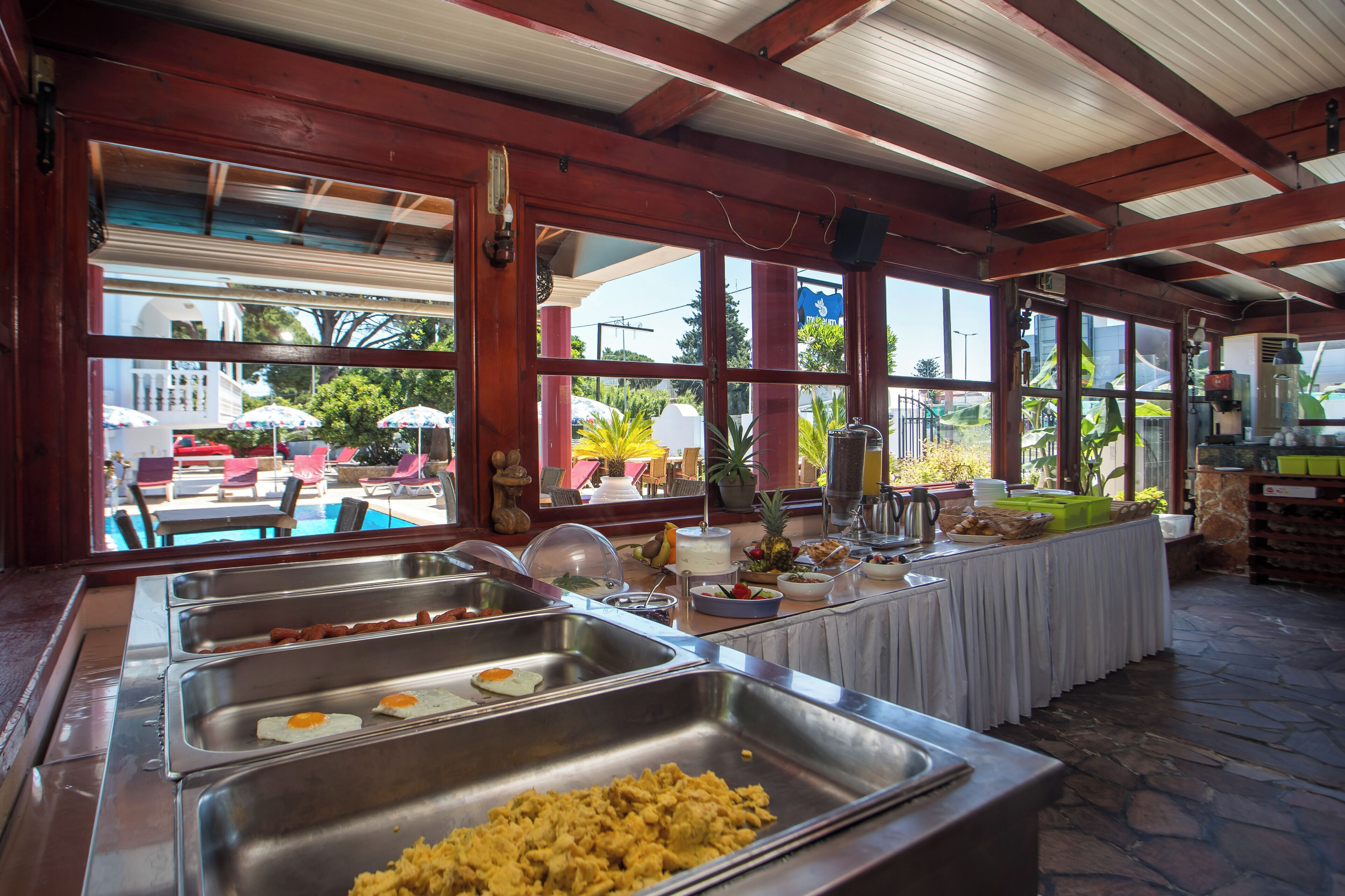 Un bufé con diversas opciones de comida, vista a la piscina y una zona de estar exterior cubierta.
