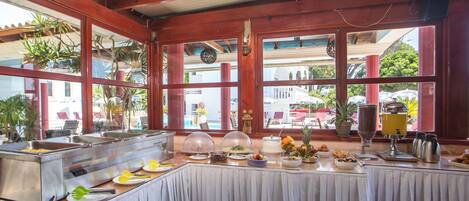 A buffet setup with a variety of food items, a beverage station, and a view of the outside through large windows.