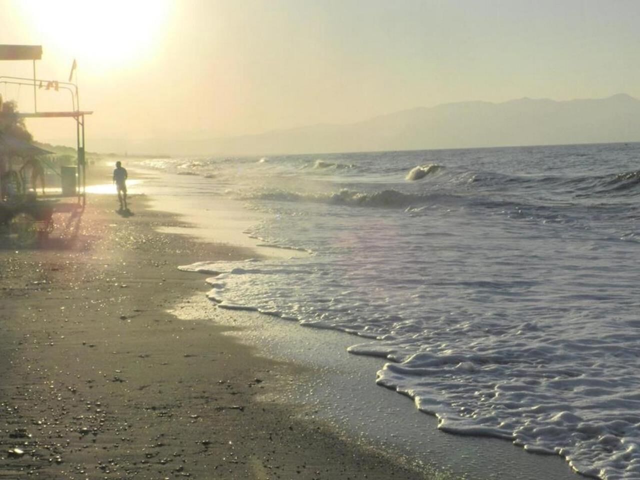 A beach with waves, a lifeguard stand, and a person walking.