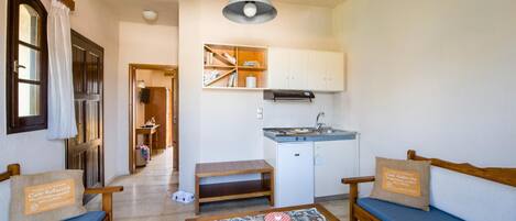 Un espacio habitable compacto con kitchenette, un sofá, una banca y una mesa estampada.