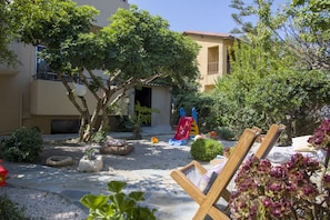 Une cour comprenant un espace de jeux pour enfants, un coin salon et un bâtiment doté d’un balcon.