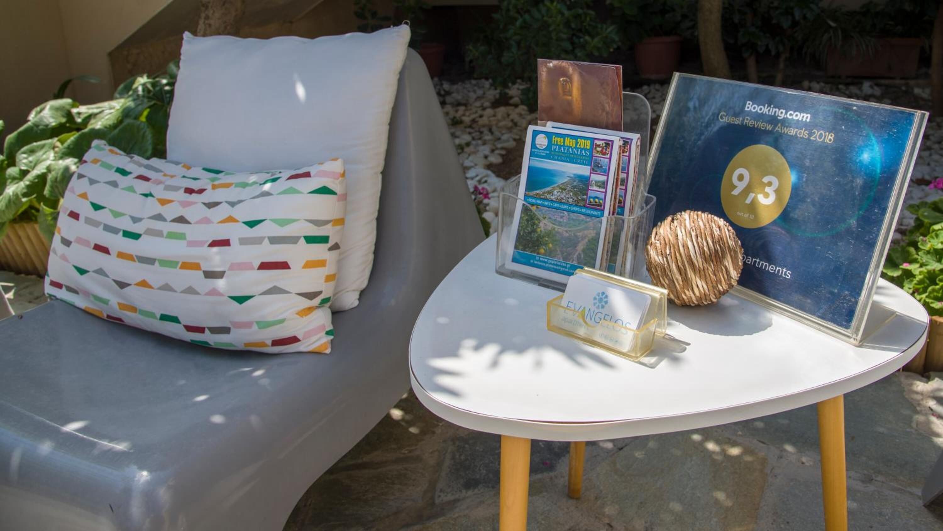 A lounge area with a white sofa, colorful pillows, a small table with a plaque, a CD, and a decorative shell.