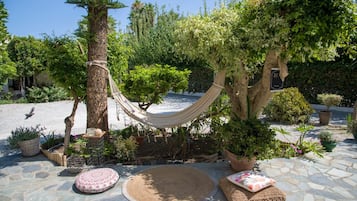 A hammock set up between two trees in a garden with potted plants and a stone floor.