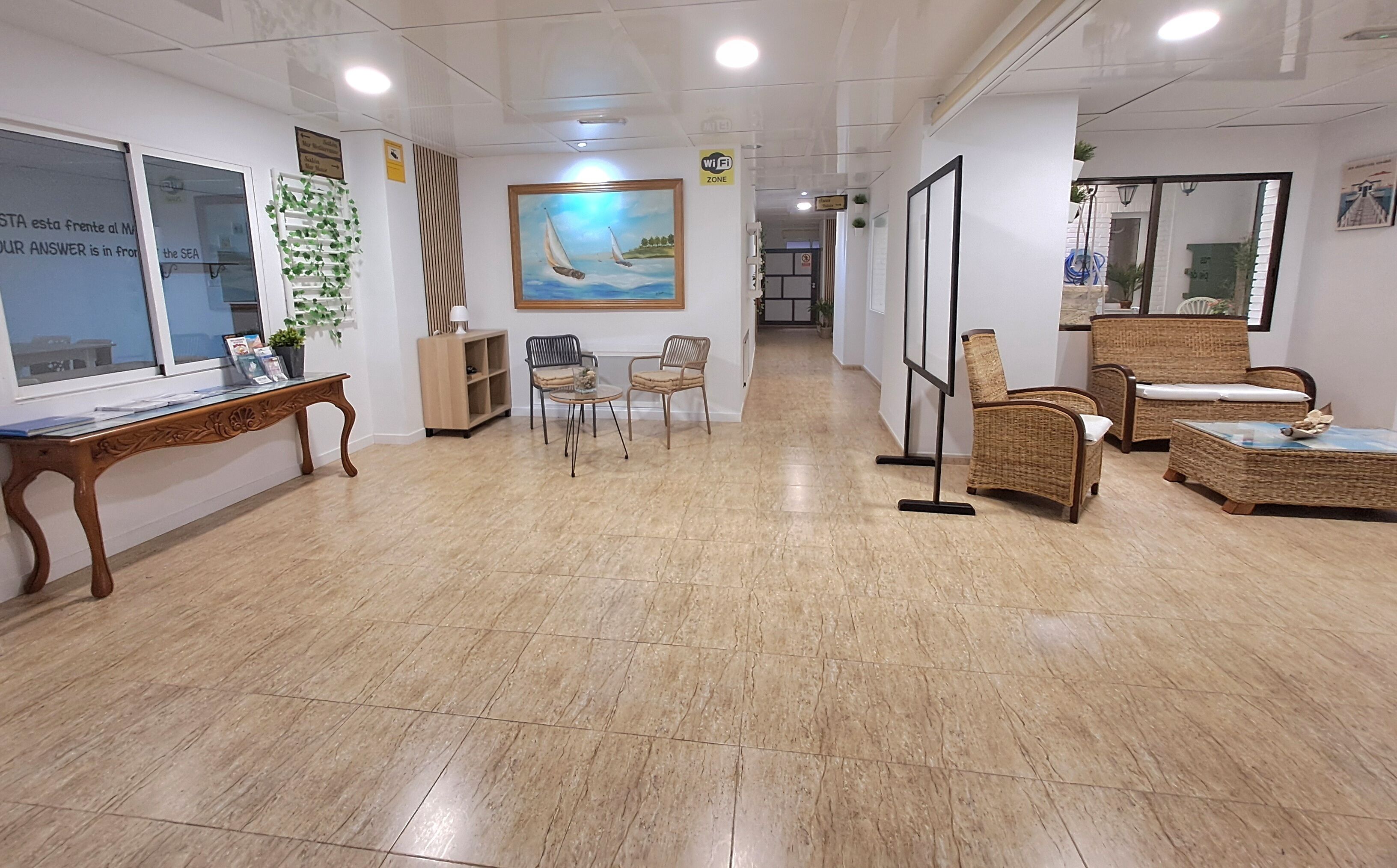 Un hall de hotel con mostrador de recepción, zona de estar y un cuadro en la pared.