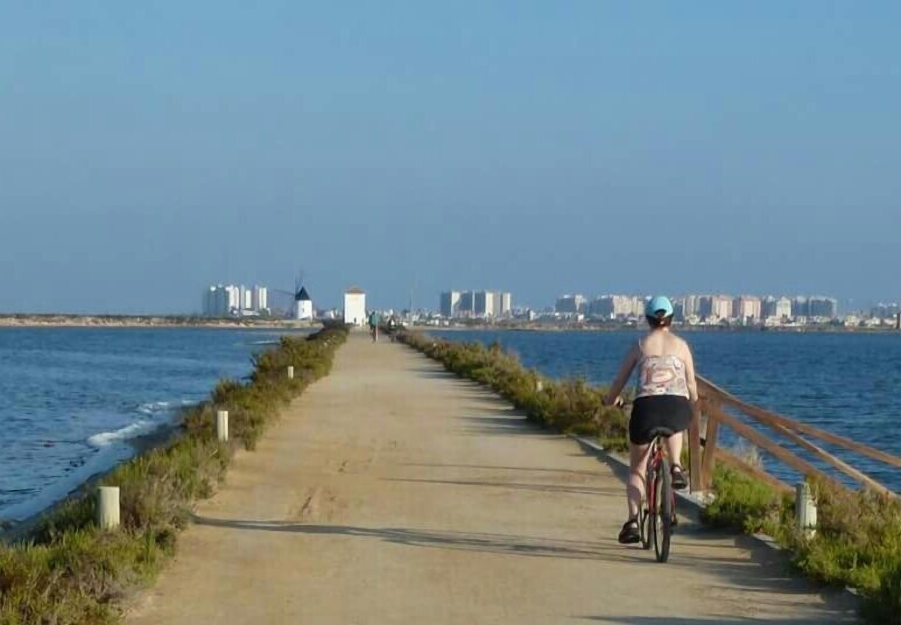 A paved path alongside a body of water with a cityscape in the background.