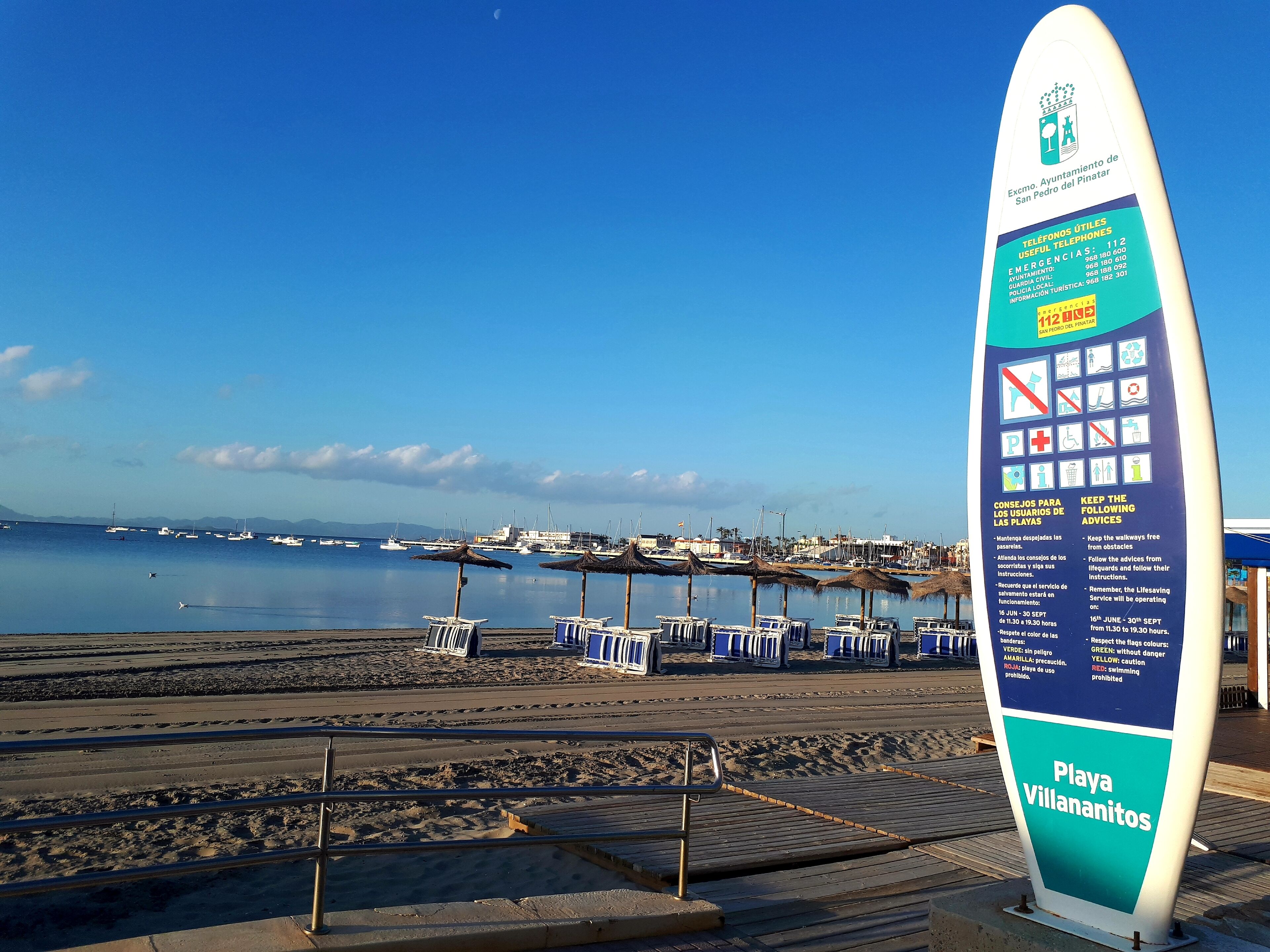A beachside sign with information for Playa Villanitos, including emergency contact numbers and beach rules.
