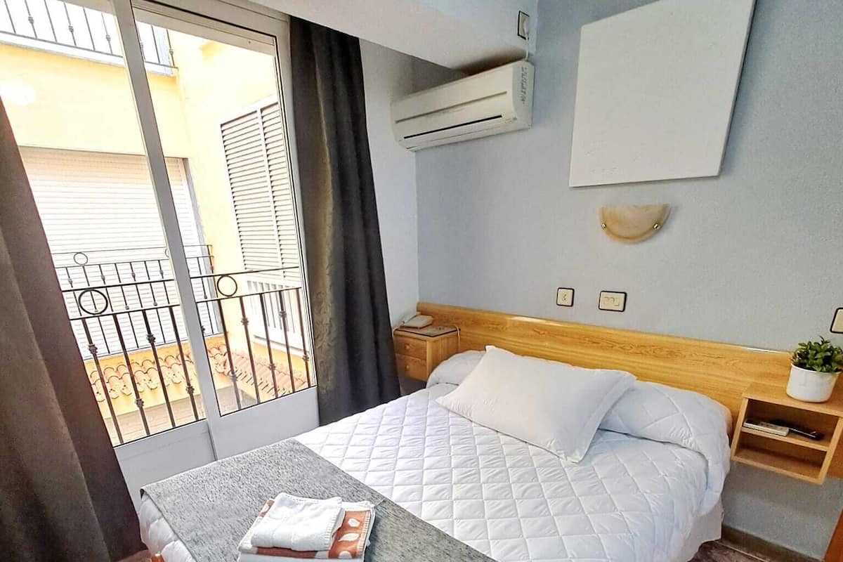 Ein Hotelzimmer mit Bett, Sessel, Nachttisch, Wand-Klimaanlage und Blick auf den Balkon.