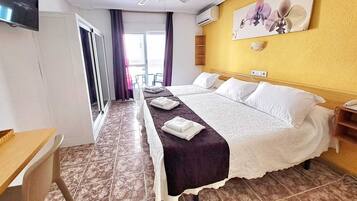 Camera d'albergo con un letto, una scrivania, una sedia, un televisore, una ventola a soffitto e una finestra con tende.