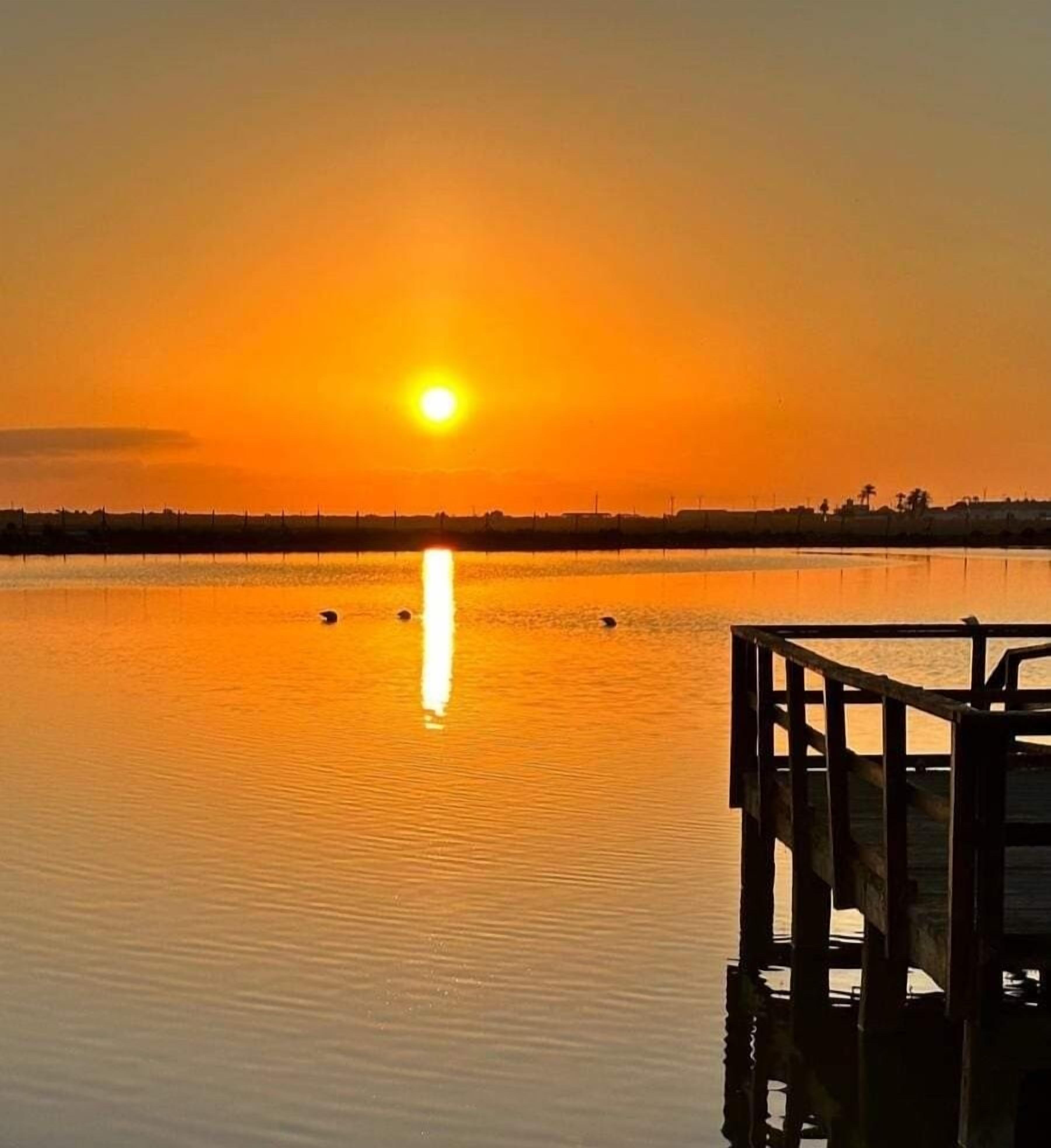 A sunset over a calm body of water with a wooden dock extending into the scene.
