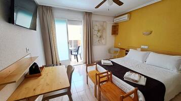 A hotel room with a bed, a desk, a chair, a table, a ceiling fan, and an air conditioning unit.