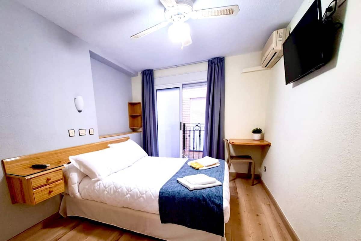 Ein Hotelzimmer mit Bett, Schreibtisch, Stuhl, Fernseher und einem Balkon mit Vorhängen.