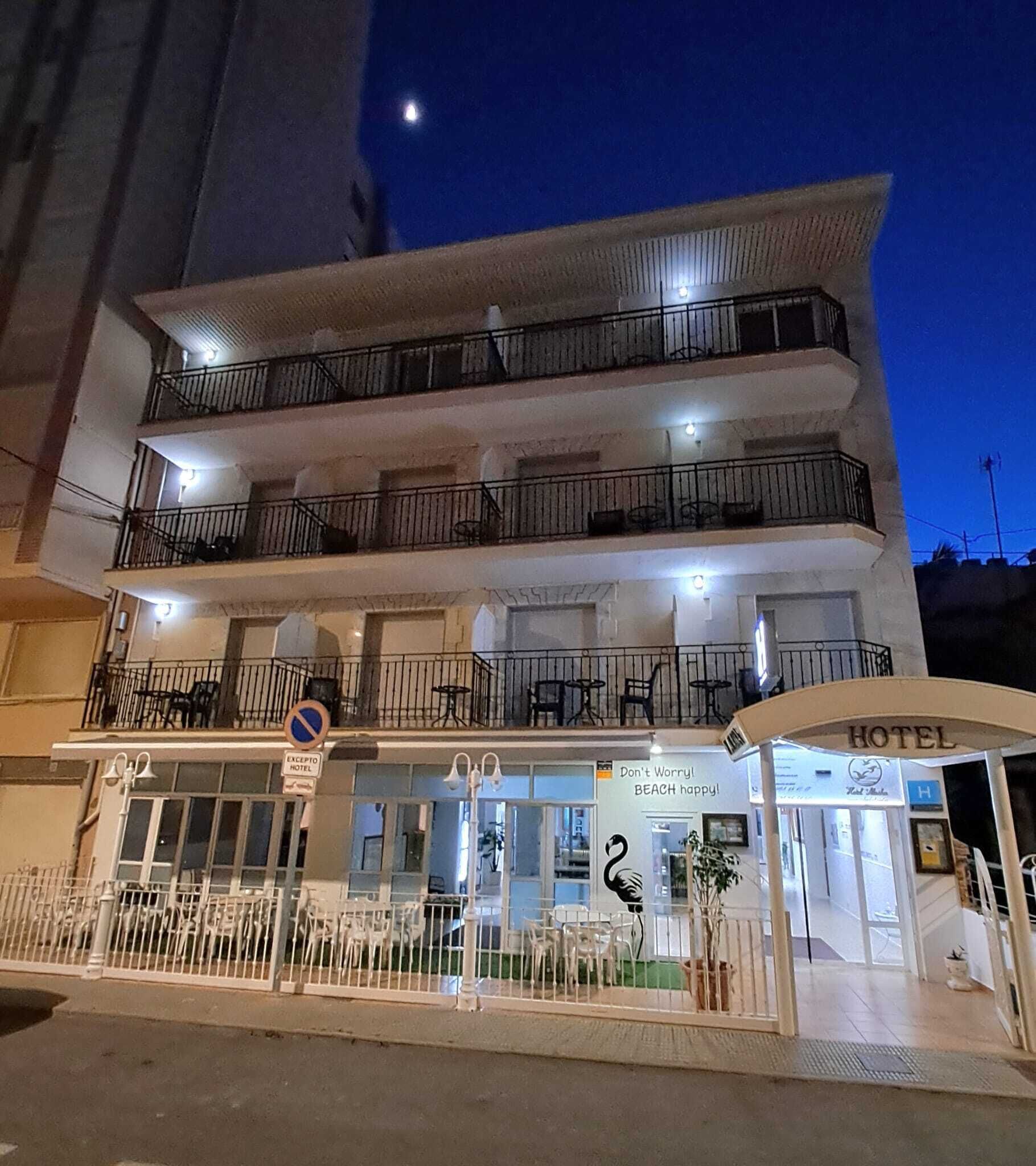 A multi-story hotel with balconies, a reception area, and a sign indicating a beach nearby.