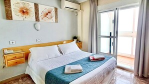 Habitación de hotel con cama, mesita de noche, aire acondicionado en la pared y ventana con cortinas.