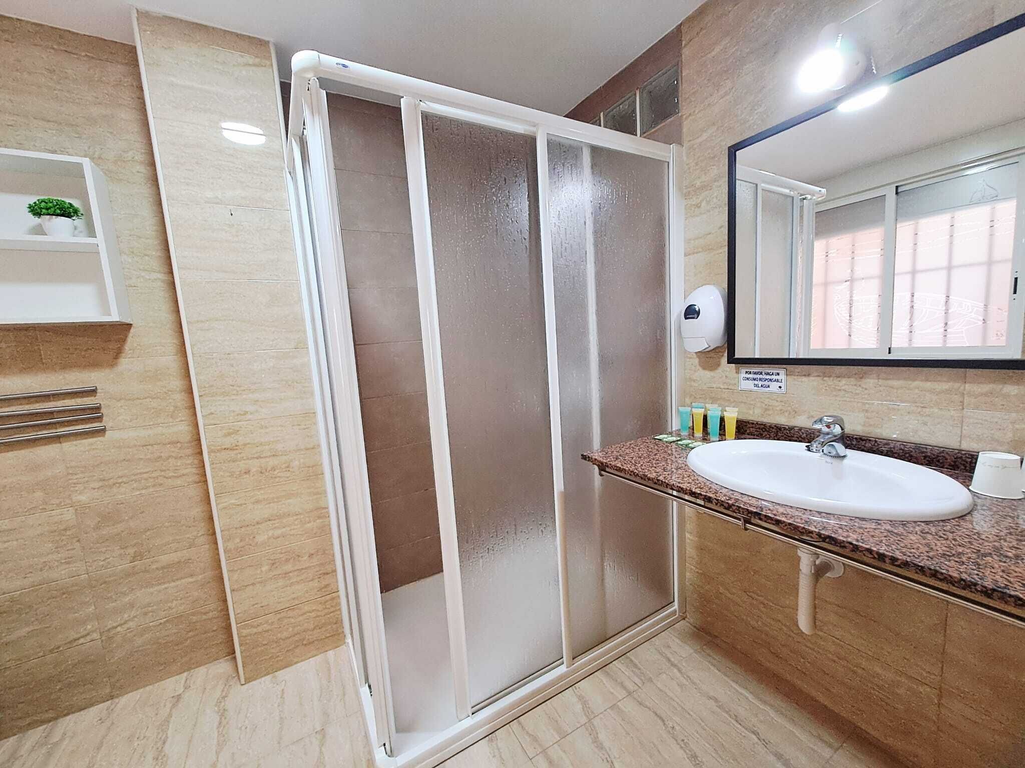 Casa de banho com chuveiro, pia, espelho e prateleira com artigos de higiene pessoal.