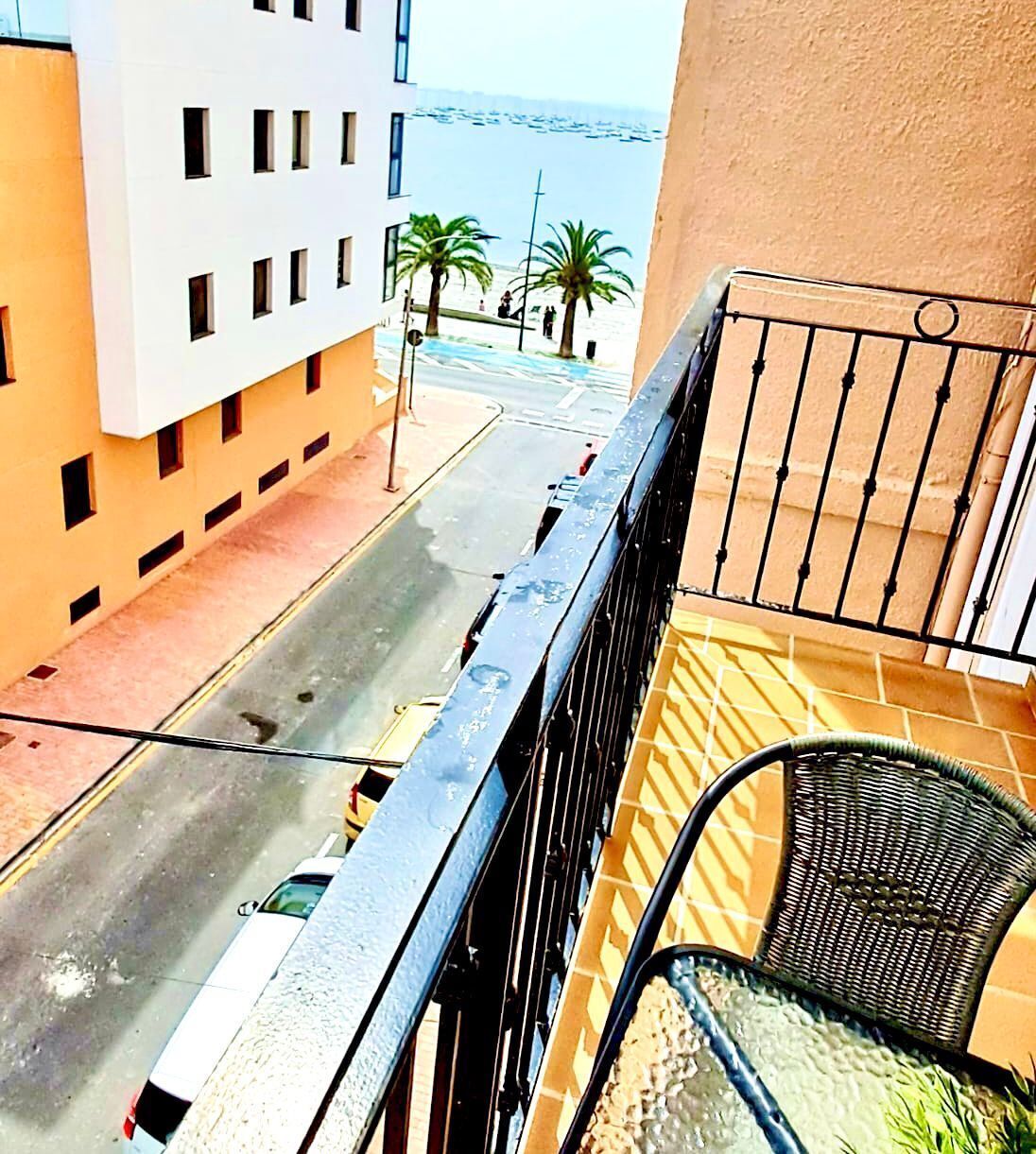 Un balcón con vistas a una calle, palmeras y un edificio.