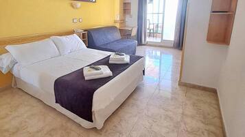 Habitación de hotel con cama, escritorio, silla, ventilador de techo y vistas al exterior.