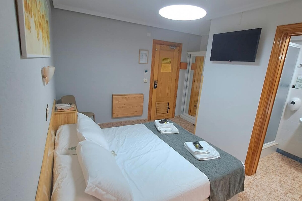 A hotel room with a bed, bedside table, and a TV mounted on the wall.