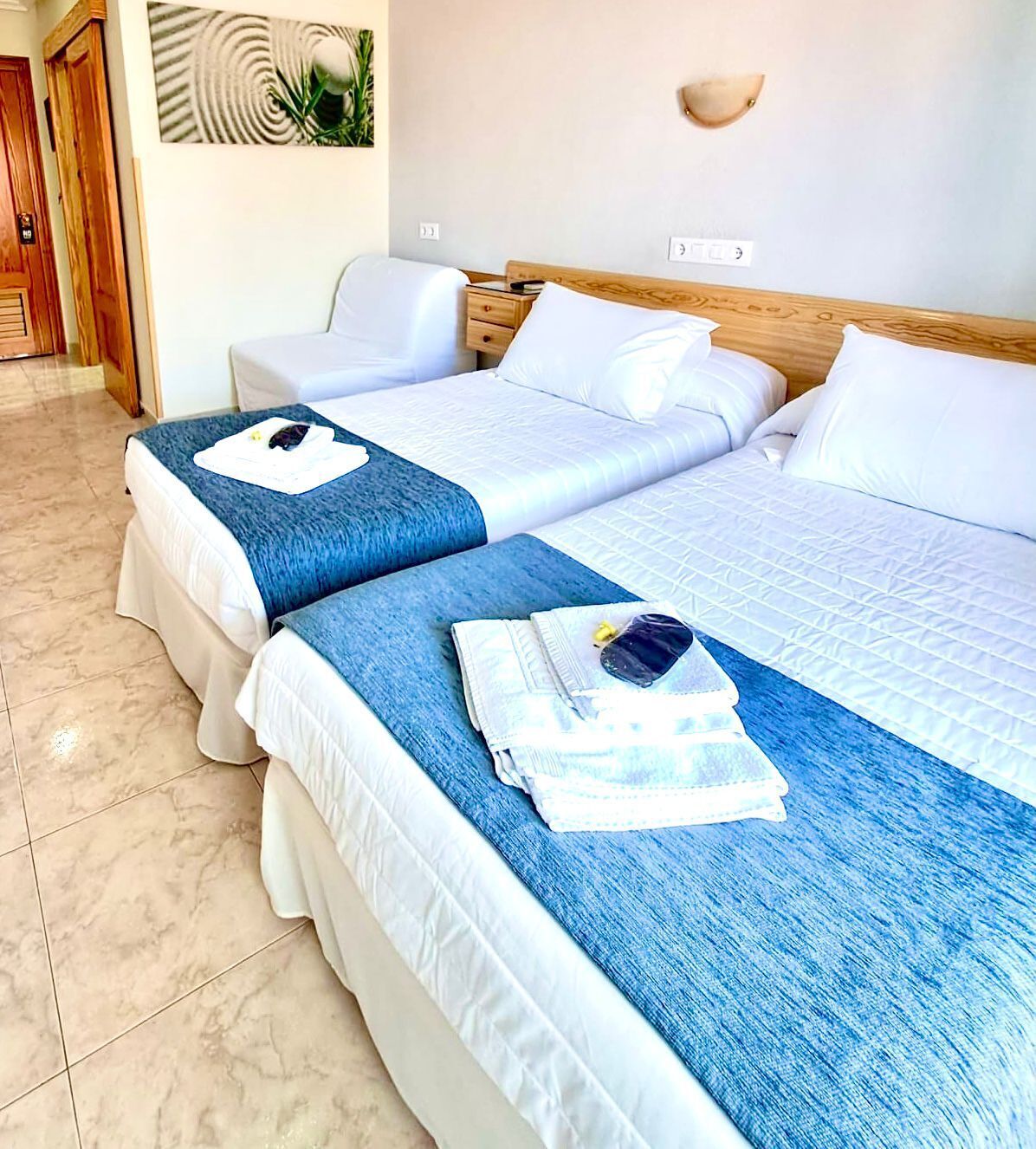 Habitación de hotel con dos camas, cabecero de madera, lámpara de pared y una puerta.