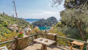 Eine Terrasse mit Tisch und Stühlen mit Blick auf eine Küstenstadt und das Meer.